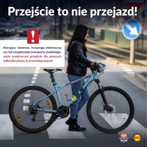 kobieta w ciemnej kurtce prowadzi niebieski rower przez przejście dla pieszych. Na gorze napis: Przejście to nie przejazd.