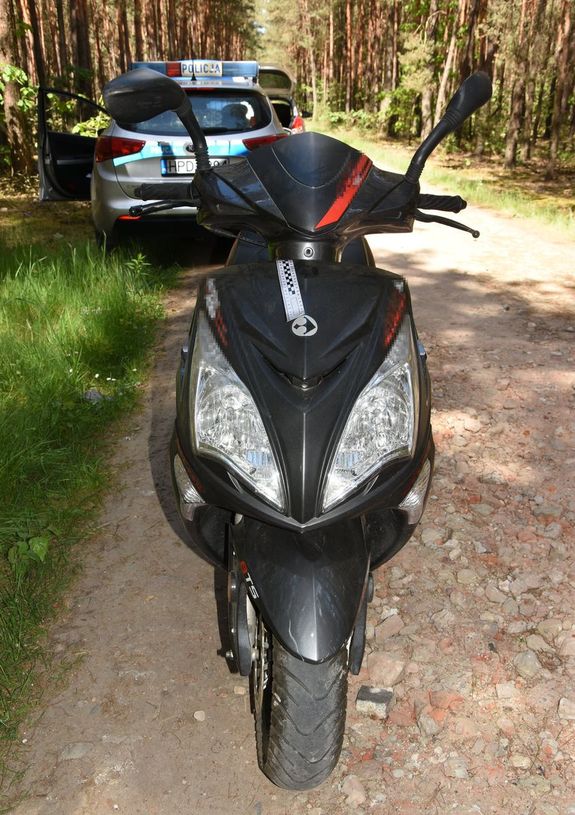 skuter w kolorze czarnym na leśnej drodze, obok stoi policjant