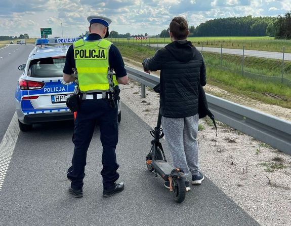 policjant stoi obok użytkownika hulajnogi na poboczu, obok radiwóz