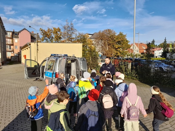 grupa dzieci stoi w pobliżu policjanta, który z nimi rozmawia